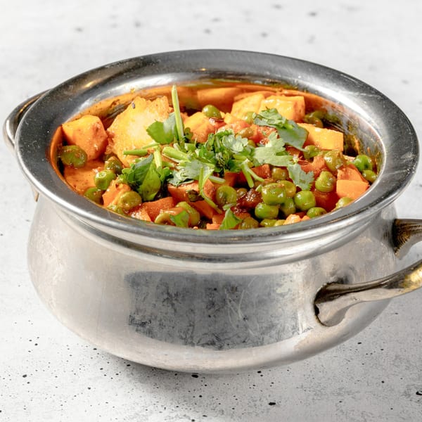 Nirvana Indian Kitchen's Aloo Matar, a potato and pea curry, garnished with fresh cilantro in a metal bowl.