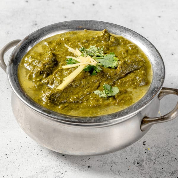 Nirvana Indian Kitchen's vibrant green Palak Paneer, garnished with fresh ginger and cilantro, in a metal serving bowl.