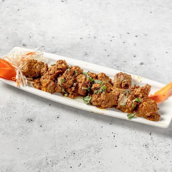 Indian lamb or beef curry, garnished with fresh herbs and shredded vegetables on a white platter.