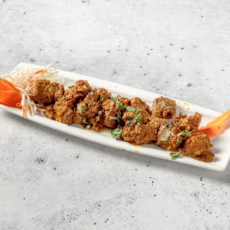 Indian lamb or beef curry, garnished with fresh herbs and shredded vegetables on a white platter.