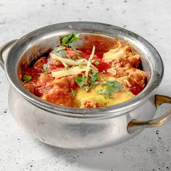Nirvana Indian Kitchen's chicken tikka masala, garnished with cilantro and ginger, in a metal serving pot.