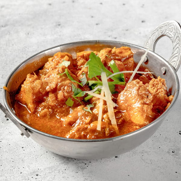 Nirvana Indian Kitchen's chicken curry, garnished with fresh cilantro and ginger, in a traditional metal bowl.
