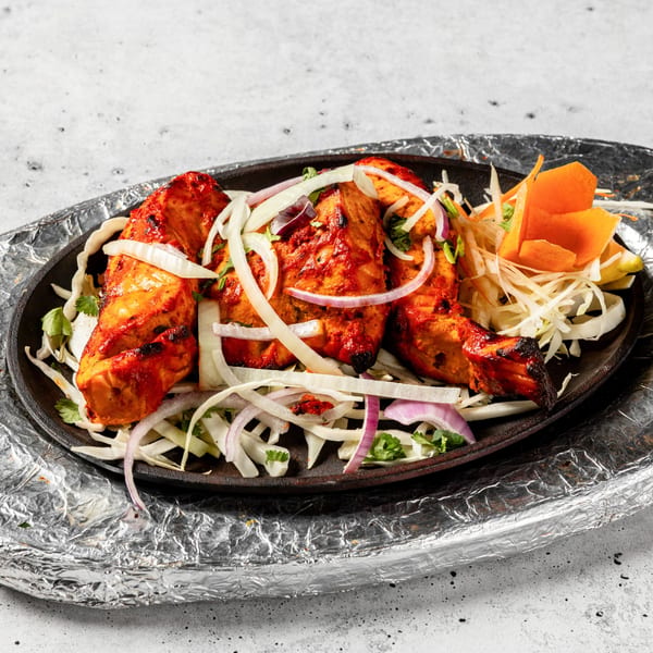Nirvana Indian Kitchen's chicken tikka, garnished with onions and carrots, served on a hot platter.