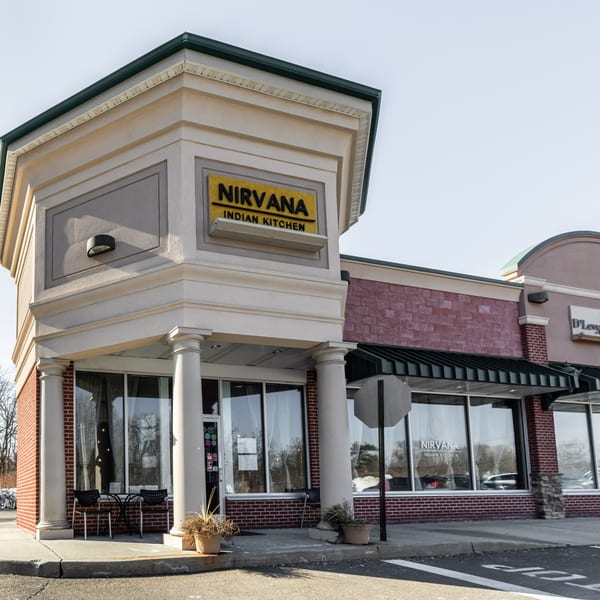 Exterior of Nirvana Indian Kitchen, a restaurant with a yellow sign, brick facade, and outdoor seating.