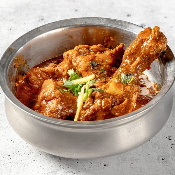 Nirvana Indian Kitchen's chicken curry, garnished with ginger and cilantro, in a metal bowl.