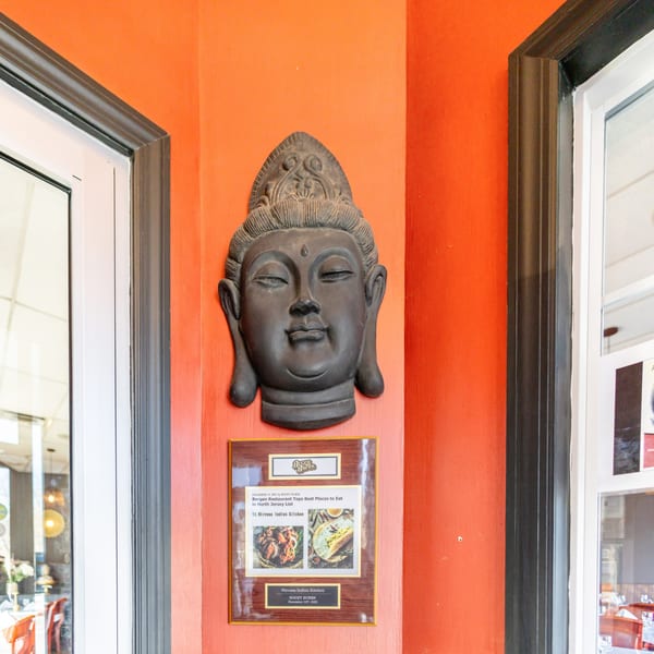 A Buddha head sculpture and a "Best Places to Eat" award plaque on an orange wall at Nirvana Indian Kitchen.