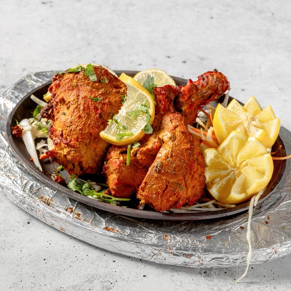 Nirvana Indian Kitchen's Tandoori Chicken, garnished with lemon wedges and fresh cilantro on a sizzling platter.