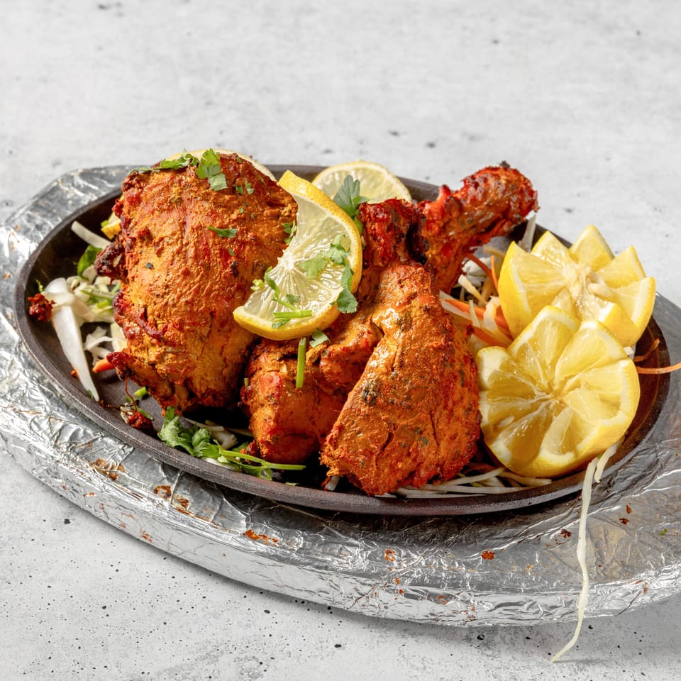 Nirvana Indian Kitchen's Tandoori Chicken, garnished with lemon wedges and fresh cilantro on a sizzling platter.