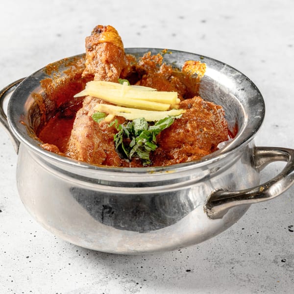 Nirvana Indian Kitchen's chicken curry, garnished with fresh ginger and mint, in a metal serving bowl.