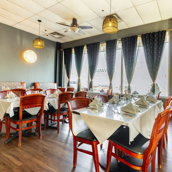 Nirvana Indian Kitchen dining room with set tables, wooden chairs, and large windows with dark curtains.