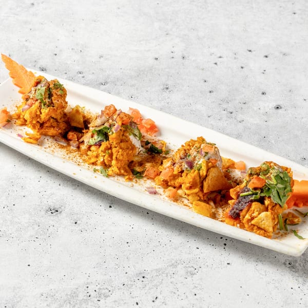 Four servings of Indian chaat, topped with cilantro, diced tomatoes, and onions, on a white platter.
