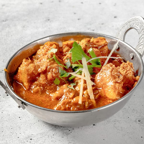 Nirvana Indian Kitchen's chicken curry, garnished with fresh cilantro and ginger, served in a metal bowl.