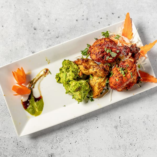 A white rectangular plate with three types of Indian chicken tikka and sauces.