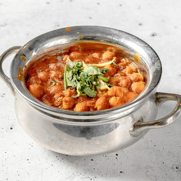 Nirvana Indian Kitchen's Chana Masala, a chickpea curry, garnished with fresh cilantro in a silver bowl.