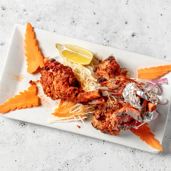 Nirvana Indian Kitchen's Tandoori Chicken, garnished with lemon, shredded cabbage, and carved carrots.