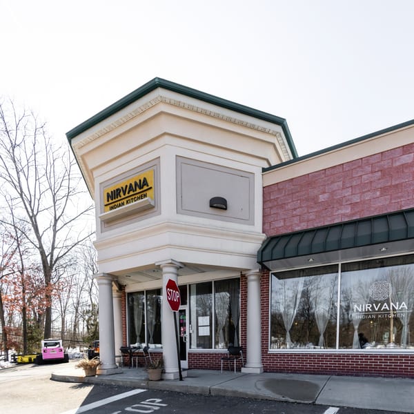Exterior of Nirvana Indian Kitchen, a brick building with a black awning and a yellow sign.