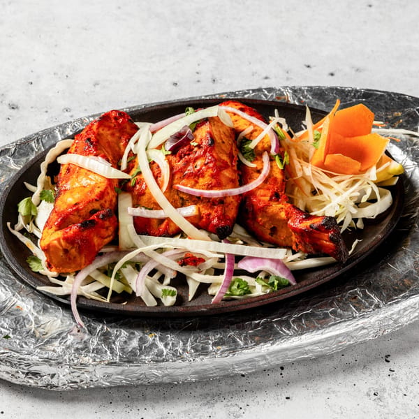 Nirvana Indian Kitchen's Tandoori Chicken, garnished with onions, cilantro, and carrots, served on a hot platter.