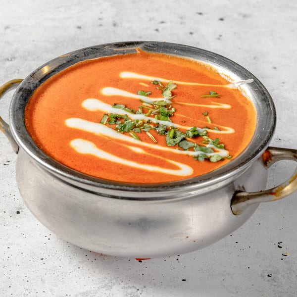 Nirvana Indian Kitchen's butter chicken in a metal serving bowl, garnished with cream swirls and cilantro.