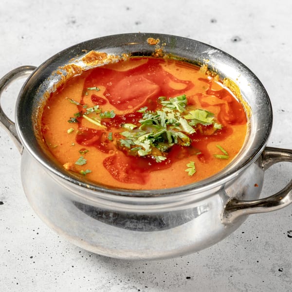 A close-up of a vibrant orange Indian curry, garnished with fresh cilantro, in a silver serving pot.