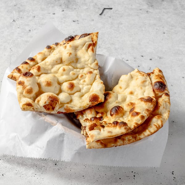 Freshly baked Indian naan bread with charred spots, served in a white paper-lined basket.