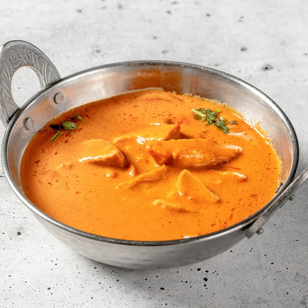 Nirvana Indian Kitchen's butter chicken, a rich orange curry with chicken pieces, served in a metal bowl.